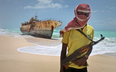 In this photo taken Sunday, Sept. 23, 2012, masked Somali pirate Hassan stands near a Taiwanese fishing vessel that washed up on shore after the pirates were paid a ransom and released the crew, in the once-bustling pirate den of Hobyo, Somalia. The empty whisky bottles and overturned, sand-filled skiffs that litter this shoreline are signs that the heyday of Somali piracy may be over - most of the prostitutes are gone, the luxury cars repossessed, and pirates talk more about catching lobsters than seizing cargo ships. (AP Photo/Farah Abdi Warsameh)